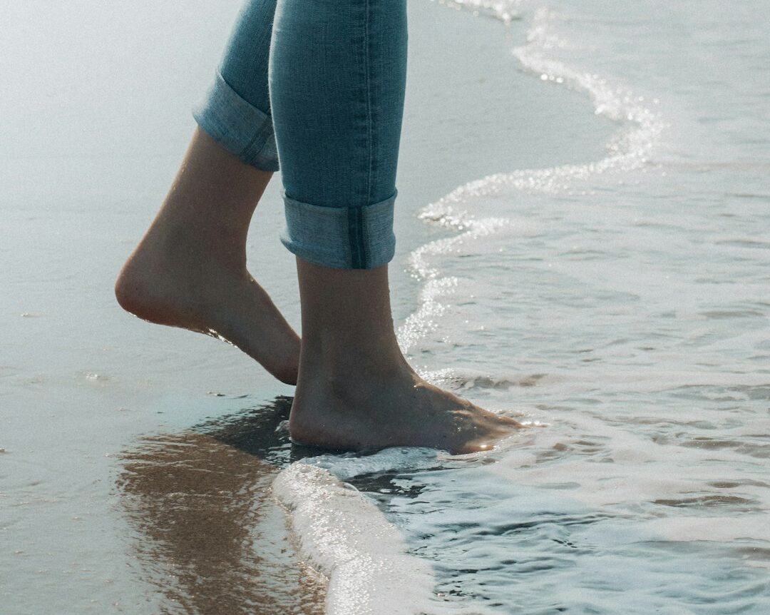 person in blue denim jeans standing on beach shore during daytime